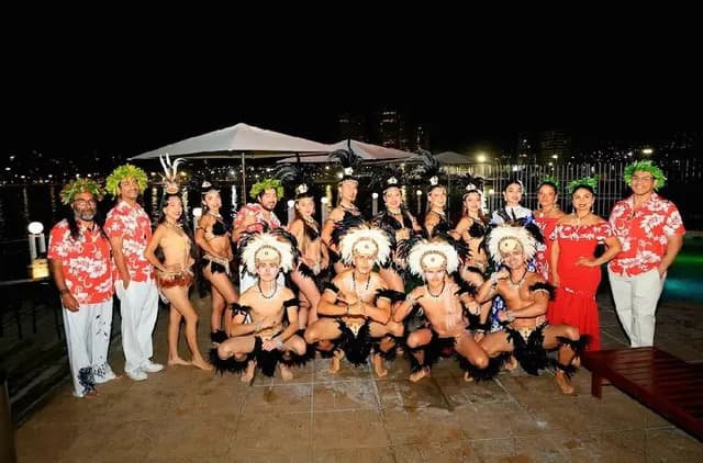 Músicos con camisas floreadas y bailarines con vestuario Rapa Nui posando de noche